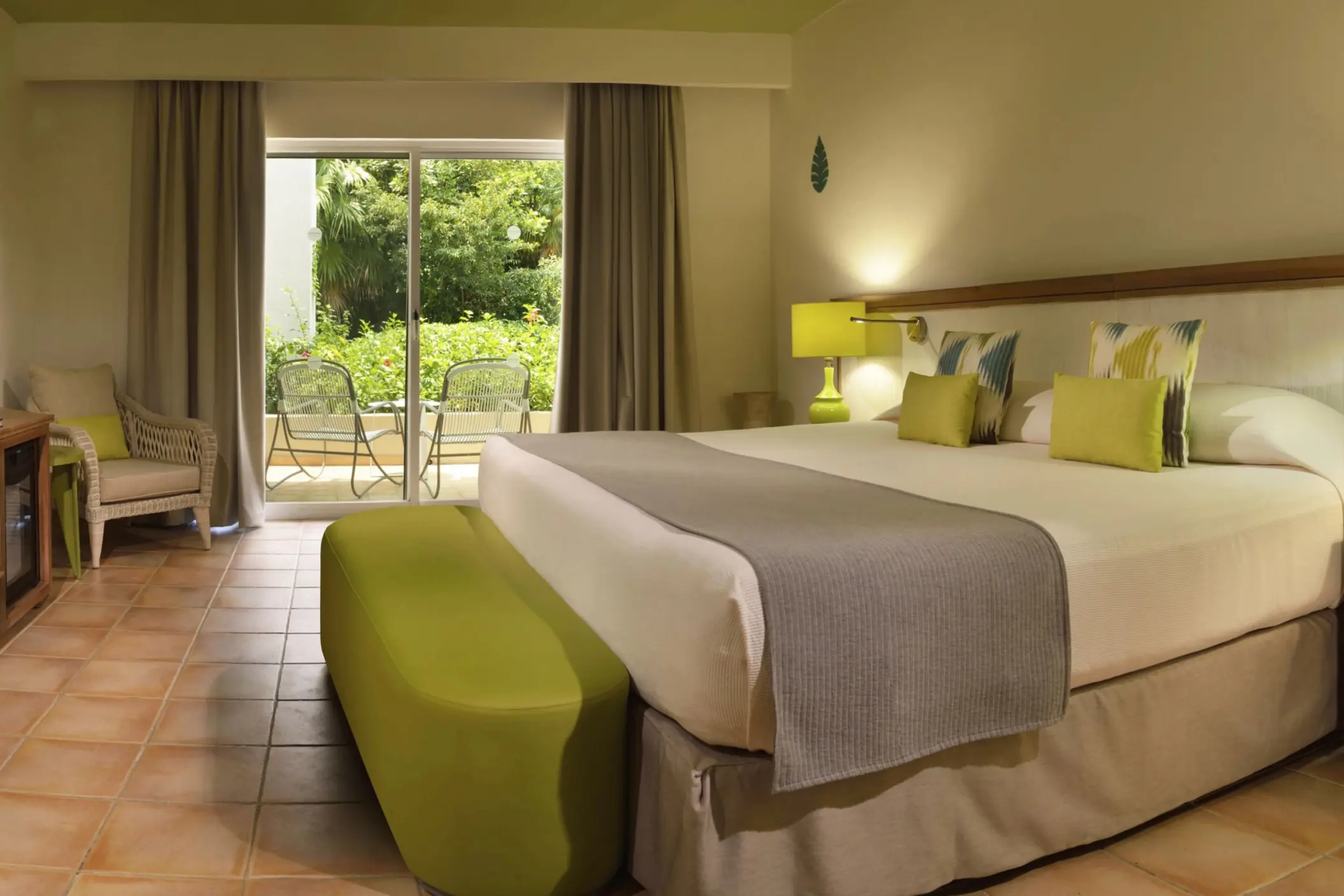 A cozy Privileged Superior suite at Catalonia Playa Maroma with a large bed, a green ottoman, and a sliding door leading to a balcony.