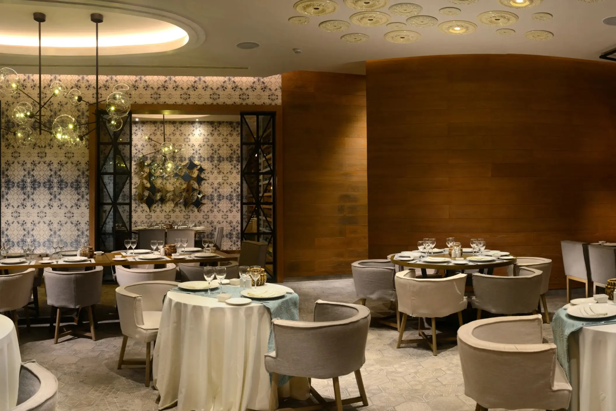 A stylish restaurant interior at Catalonia Playa Maroma with elegantly set tables, patterned walls, and warm lighting.