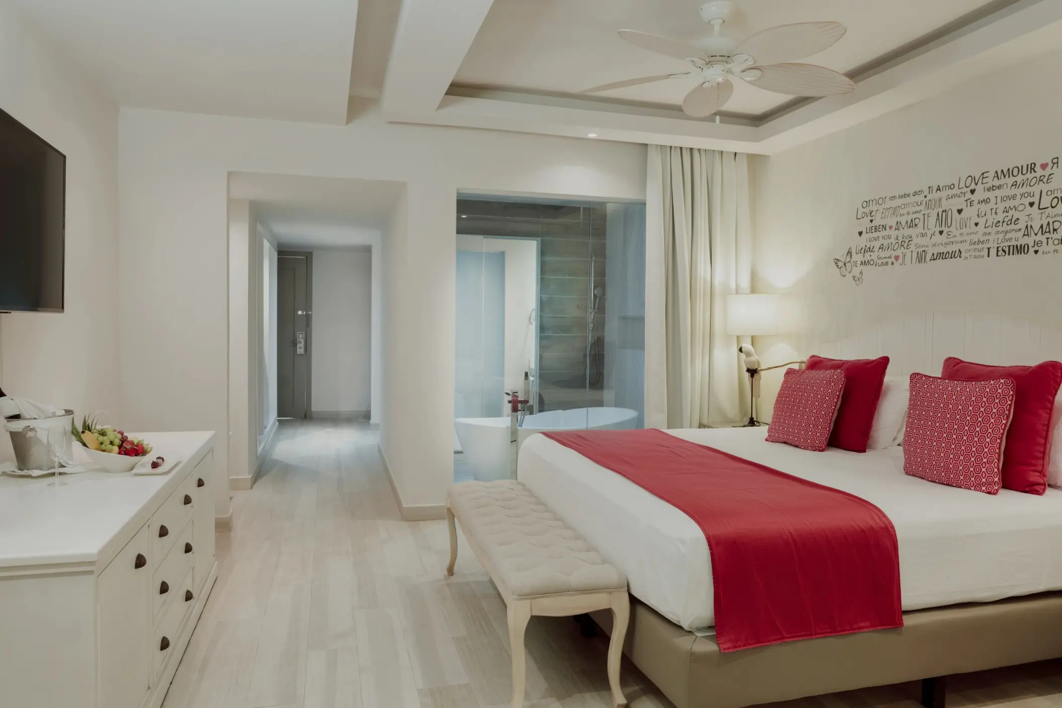 bright and spacious Romance Suite at Catalonia Playa Maroma, featuring a large bed with red accents and an open bathroom with a tub.