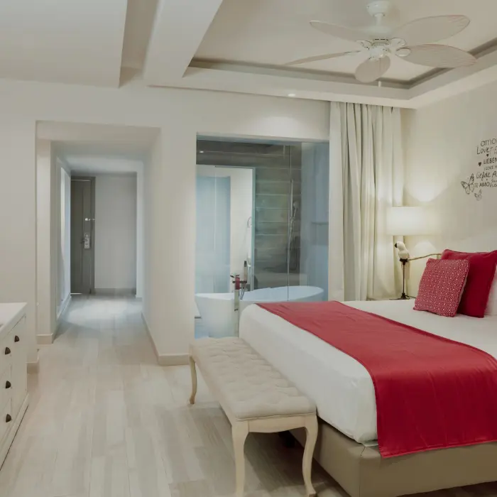 bright and spacious Romance Suite at Catalonia Playa Maroma, featuring a large bed with red accents and an open bathroom with a tub.