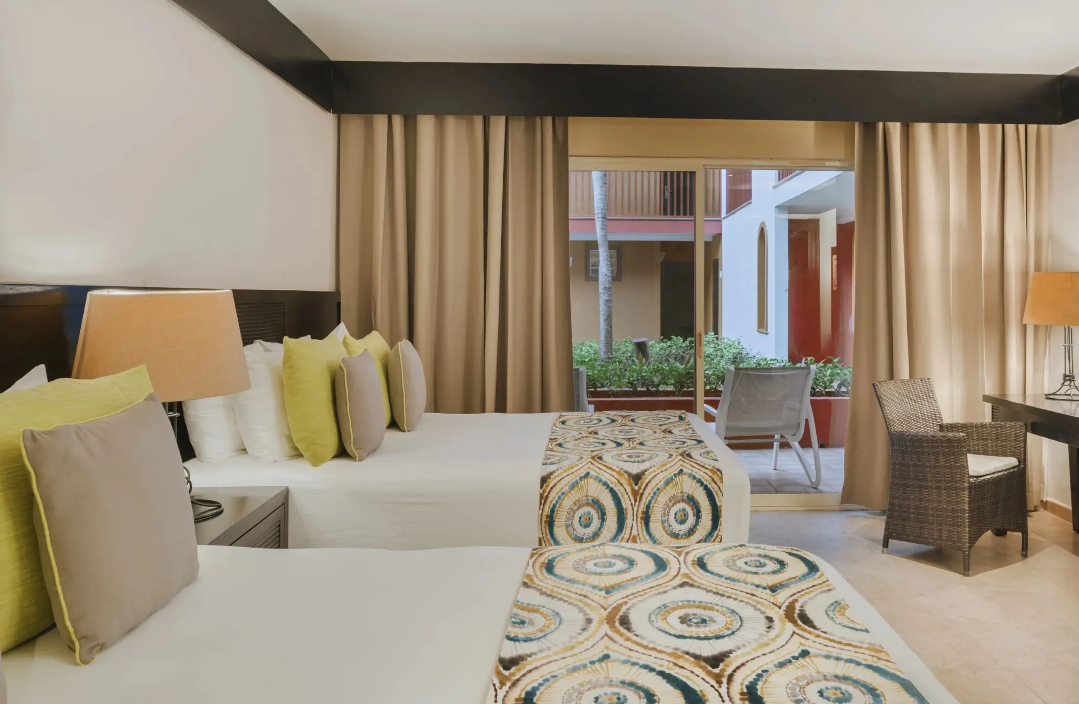A comfortable resort room at Catalonia Playa Maroma with two beds, neutral tones, and a balcony view of the exterior.