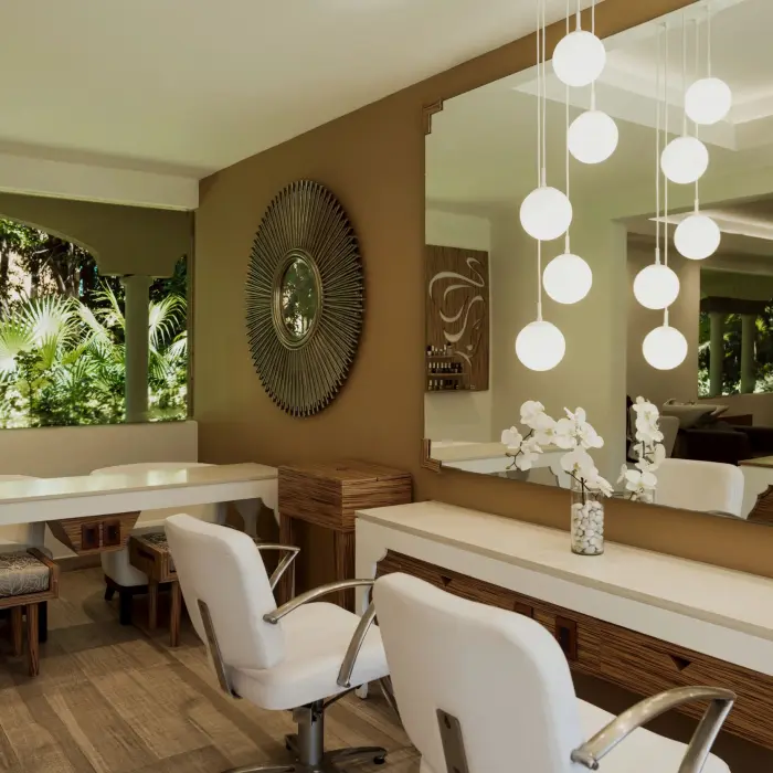 chic and modern salon at Catalonia Playa Maroma with white styling chairs, large mirrors, and decorative lighting.