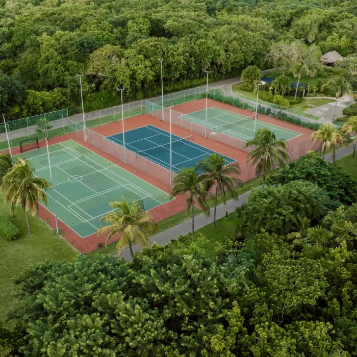 Aerial view of multiple tennis courts at Catalonia Playa Maroma, nestled within lush green tropical foliage and palm trees.