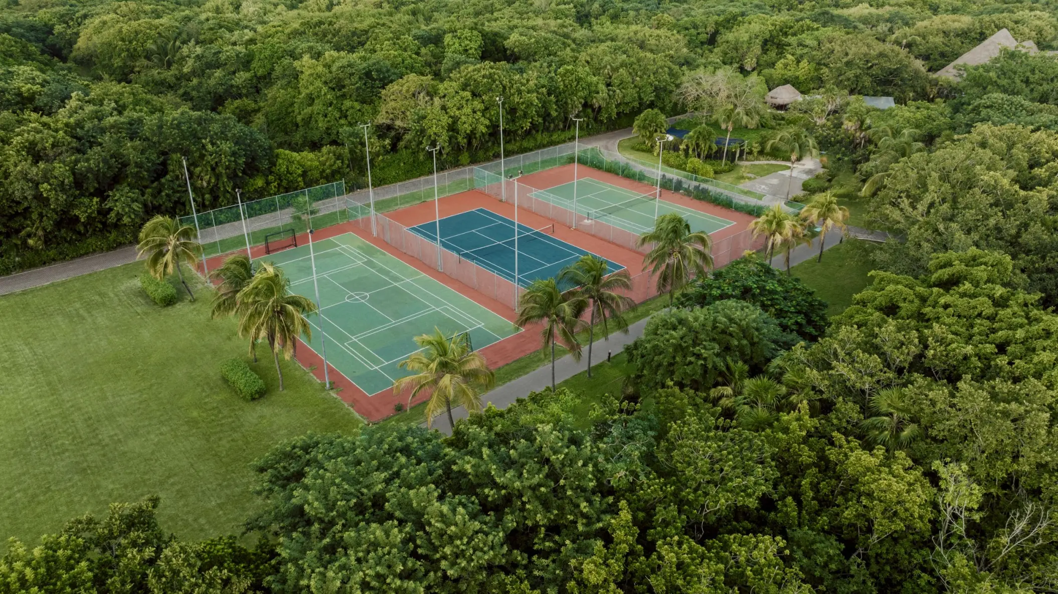 Aerial view of multiple tennis courts at Catalonia Playa Maroma, nestled within lush green tropical foliage and palm trees.