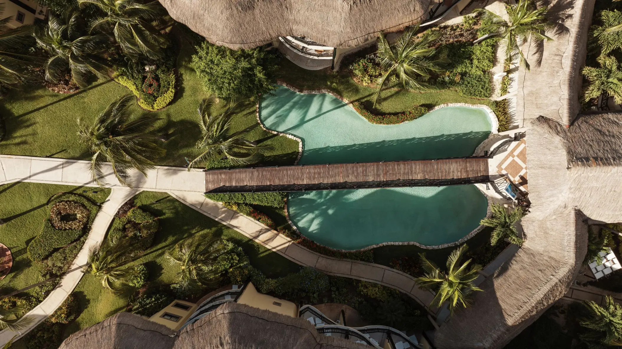A top-down aerial shot of the resort's lush gardens and a large, winding swimming pool with a bridge.