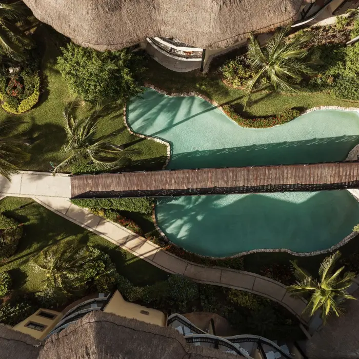 A top-down aerial shot of the resort's lush gardens and a large, winding swimming pool with a bridge.