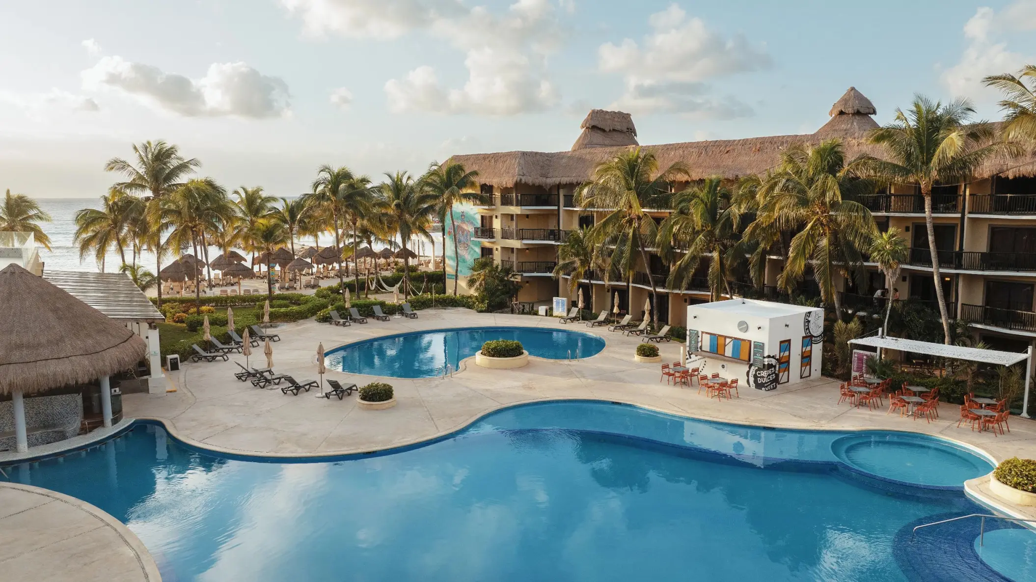 The resort buildings with a large, freeform swimming pool, palm trees, and lounge chairs with the ocean beyond.