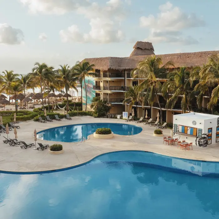 The resort buildings with a large, freeform swimming pool, palm trees, and lounge chairs with the ocean beyond.