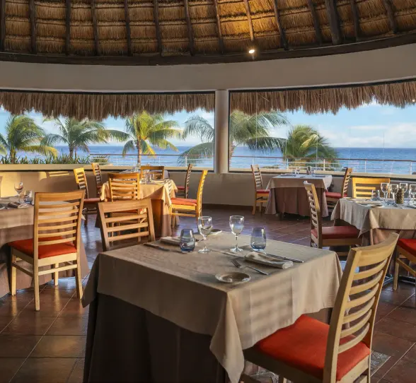 An elegant, round restaurant with a thatched roof and large windows, offering a panoramic view of the ocean.