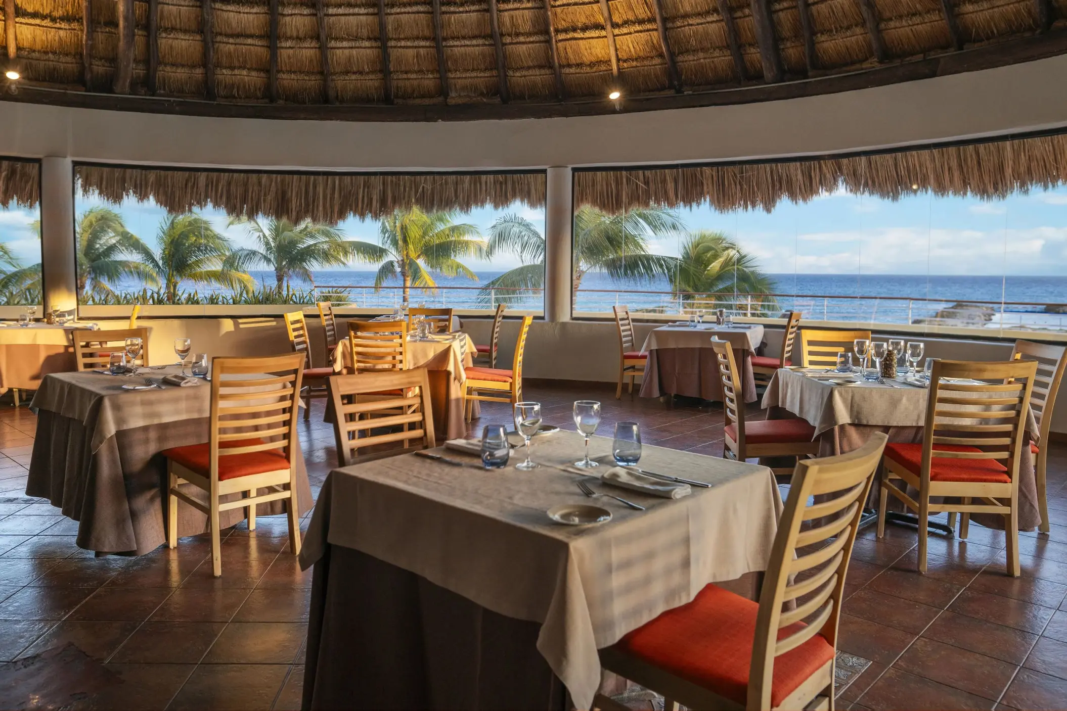 An elegant, round restaurant with a thatched roof and large windows, offering a panoramic view of the ocean.
