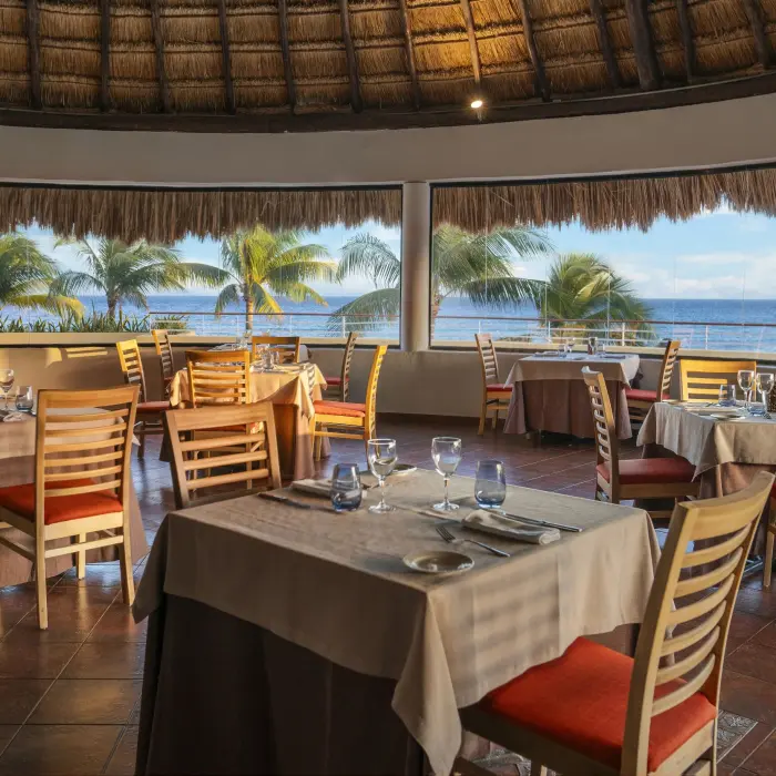 An elegant, round restaurant with a thatched roof and large windows, offering a panoramic view of the ocean.