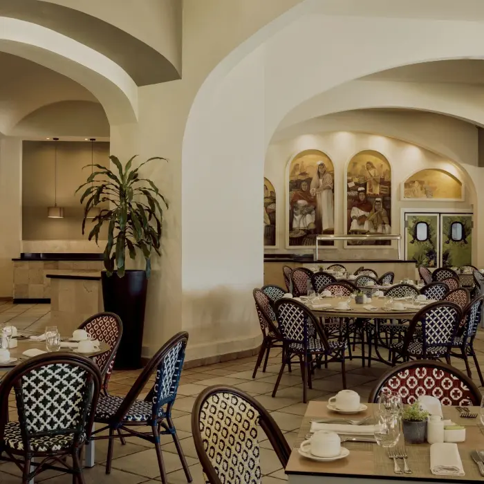 An elegant restaurant with arched doorways, round tables with decorative chairs, and murals on the walls.