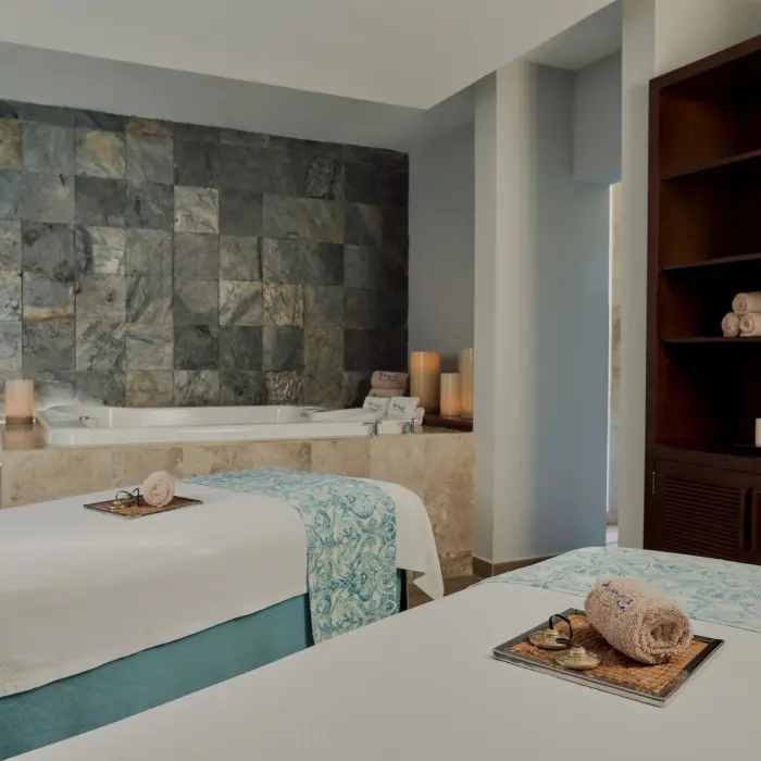A tranquil spa room with two massage beds, a jacuzzi, and decorative candles.