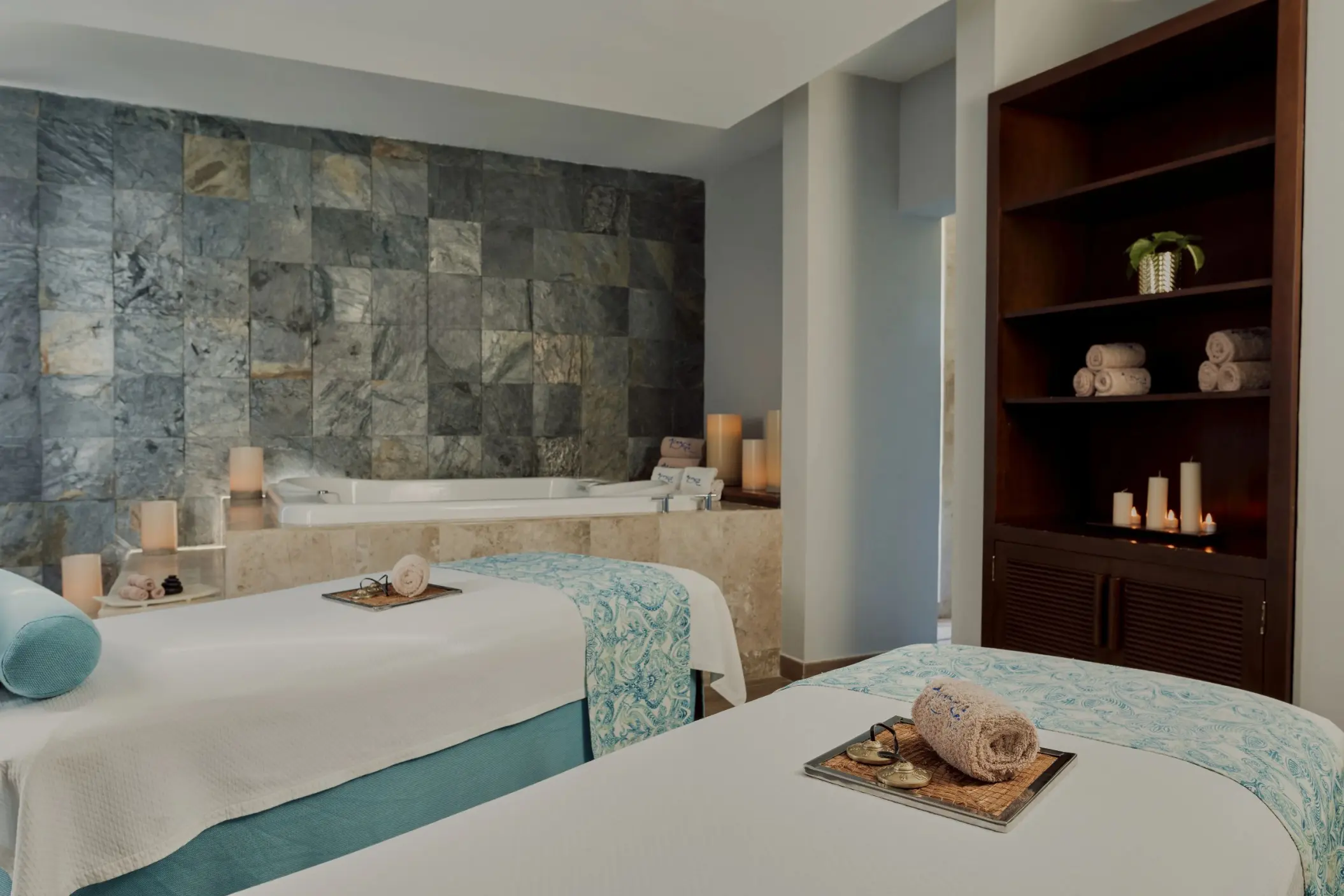 A tranquil spa room with two massage beds, a jacuzzi, and decorative candles.