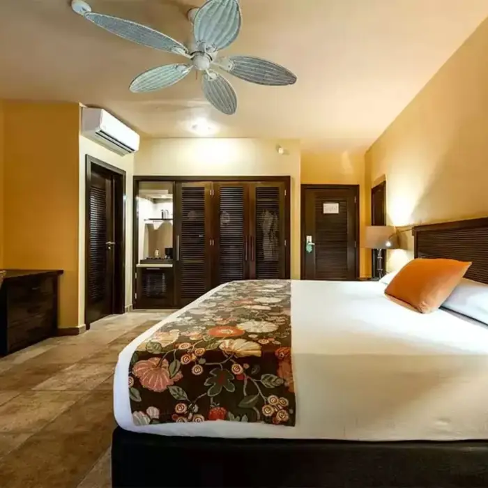 A comfortable suite with a large bed, a desk, a ceiling fan, and wooden furniture.