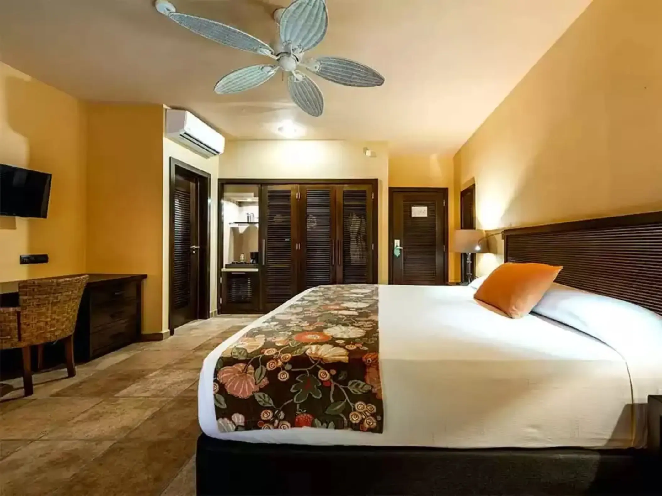 A comfortable suite with a large bed, a desk, a ceiling fan, and wooden furniture.