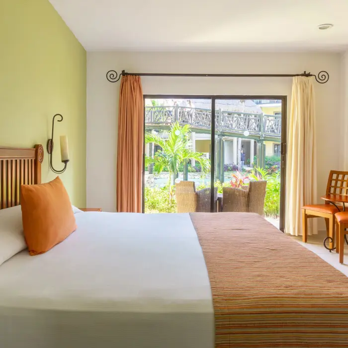 A bright suite with a large bed, garden view balcony, and traditional wooden furniture.