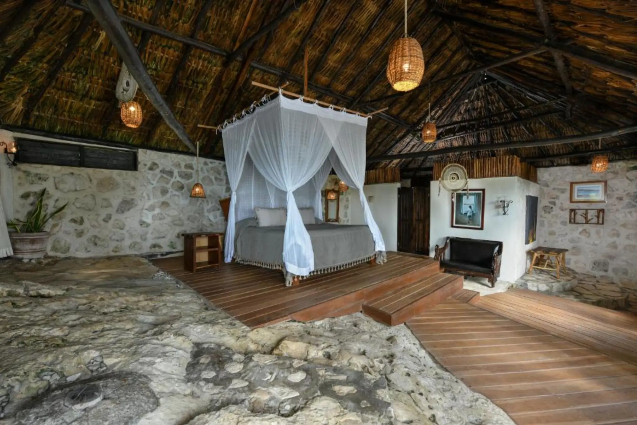 The interior of a unique suite with a canopy king bed, thatched roof, and natural stone and wood elements.
