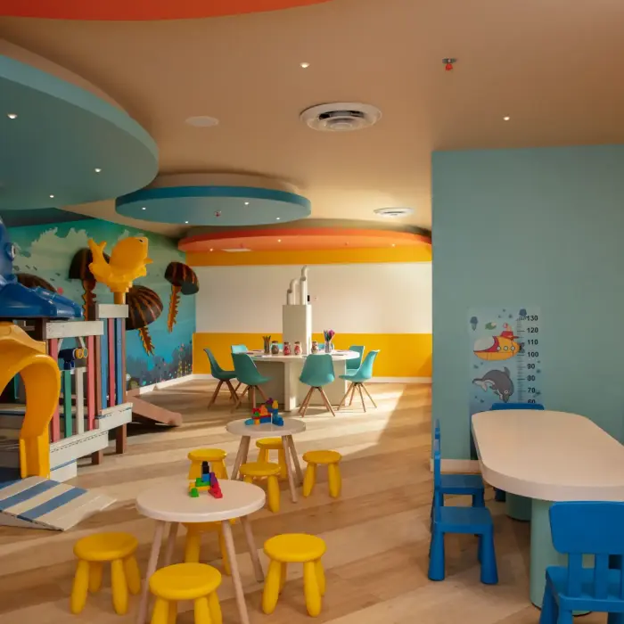 Bright indoor kids' play area with colorful tables, ocean-themed walls, and a soft structure with sea animal elements.