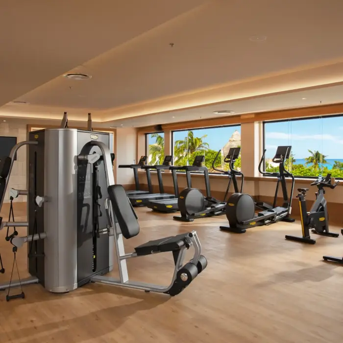 Modern fitness center with cardio machines and weight equipment, large windows offering tropical ocean views.