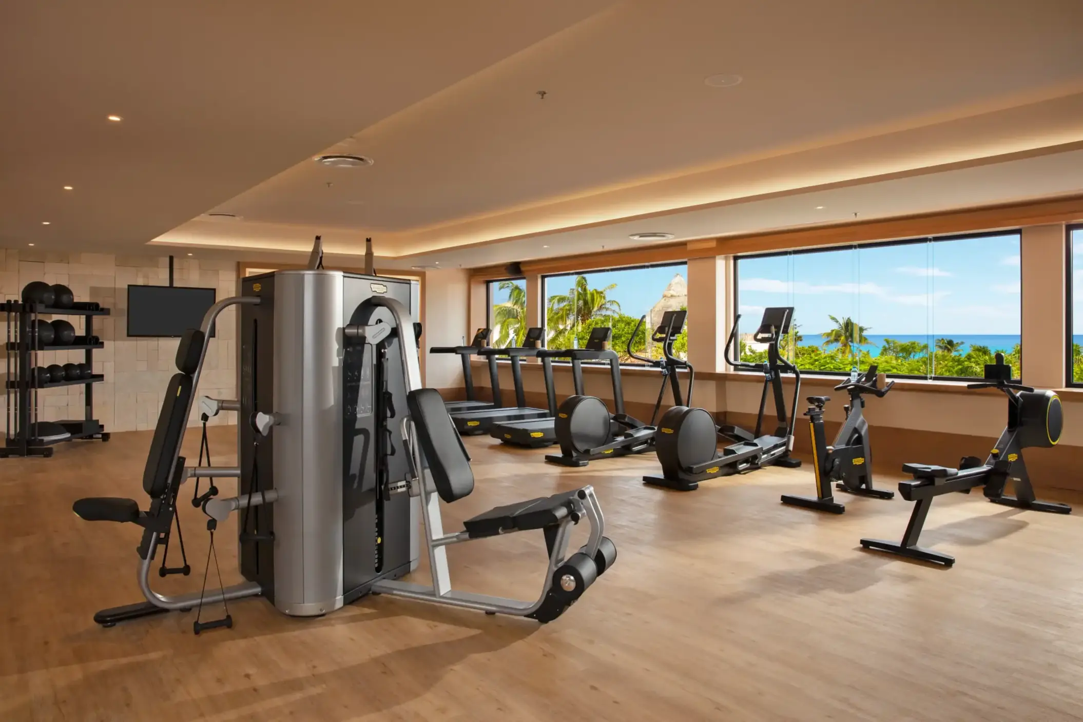 Modern fitness center with cardio machines and weight equipment, large windows offering tropical ocean views.