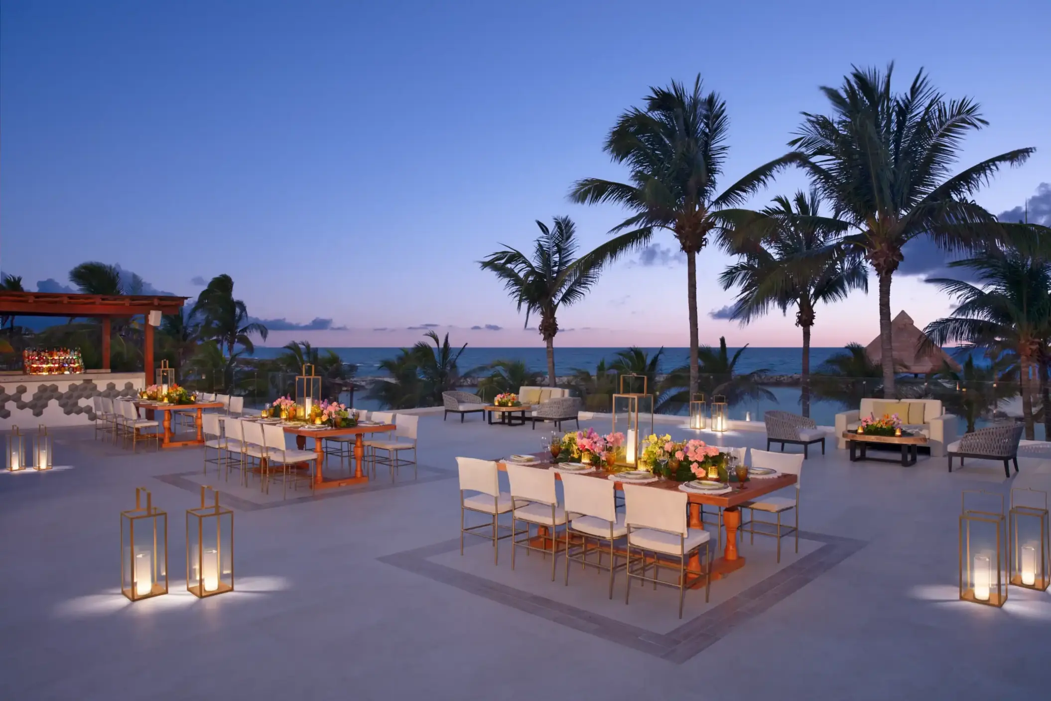 Luxury beachfront lounge area at Dreams Aventuras with modern furniture, lanterns, and palm tree setting.