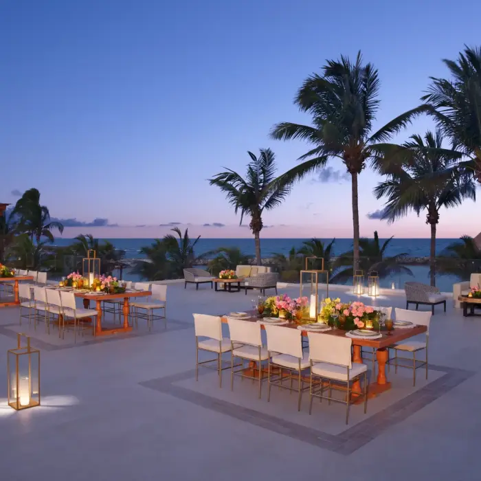 Luxury beachfront lounge area at Dreams Aventuras with modern furniture, lanterns, and palm tree setting.