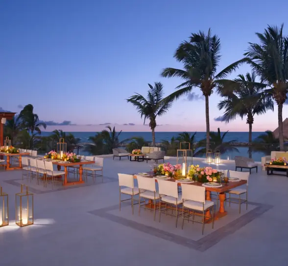 Luxury beachfront lounge area at Dreams Aventuras with modern furniture, lanterns, and palm tree setting.