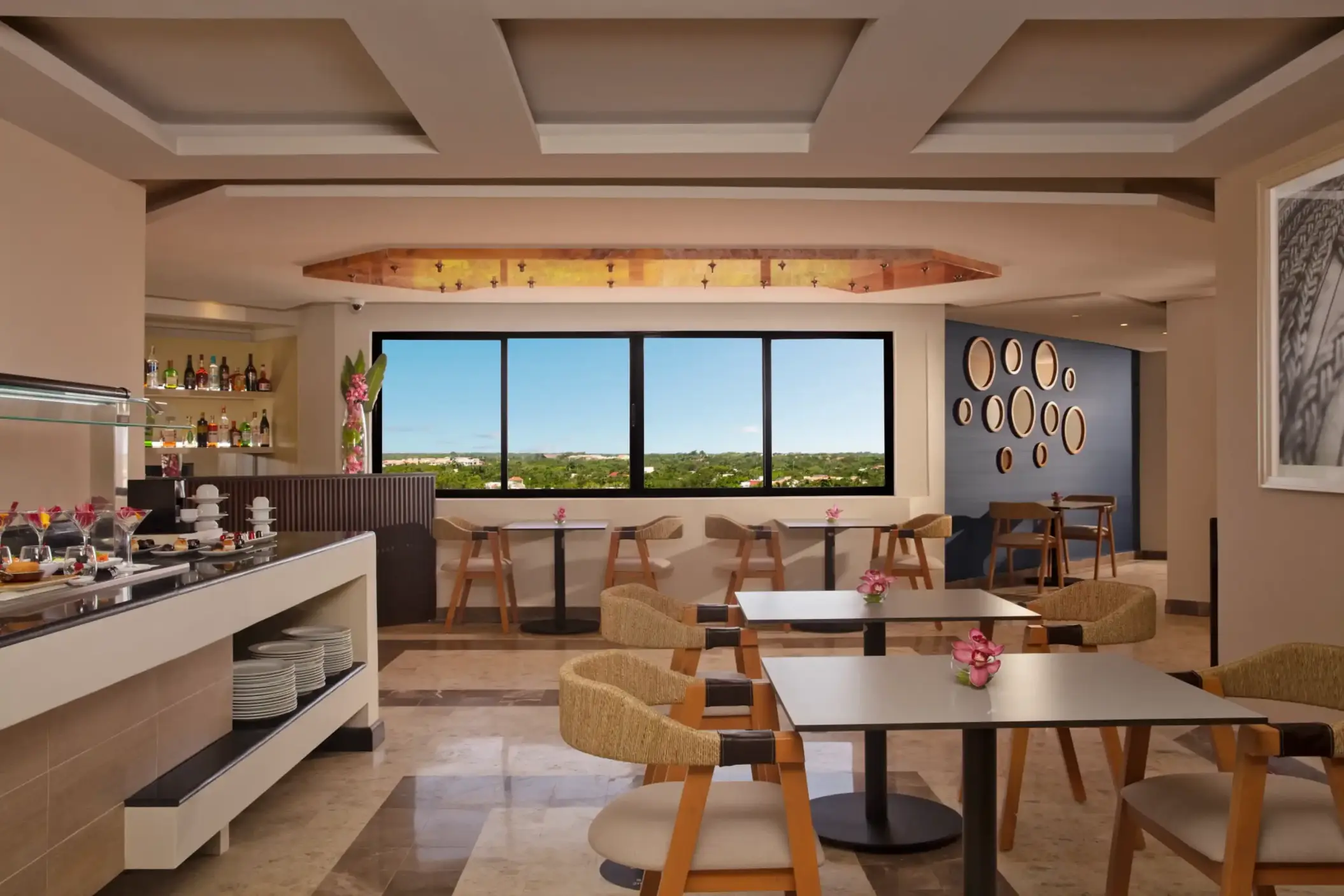 Relaxed lounge area with buffet setup, modern decor, window seating, and sweeping views of green landscape.