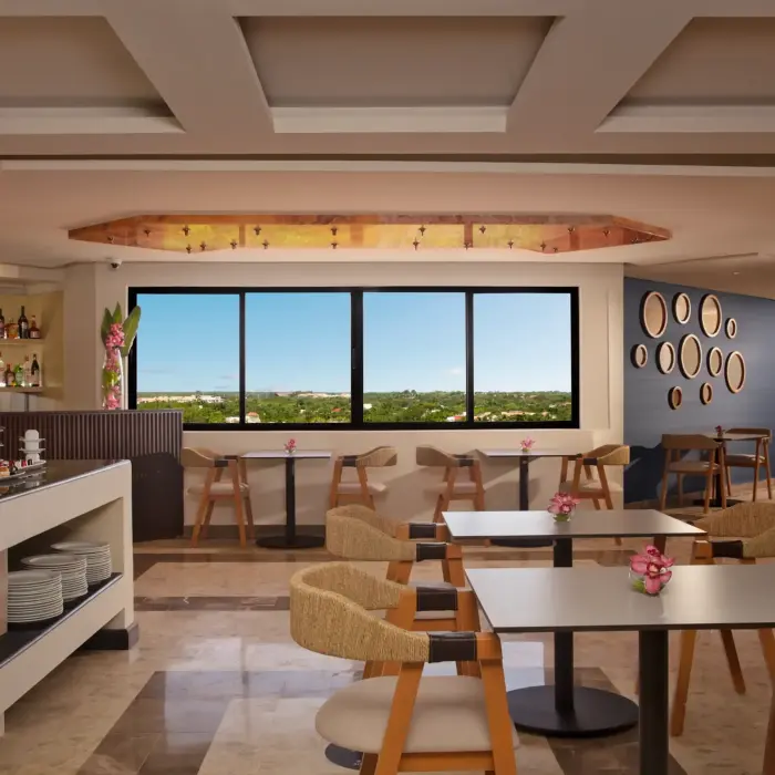 Relaxed lounge area with buffet setup, modern decor, window seating, and sweeping views of green landscape.