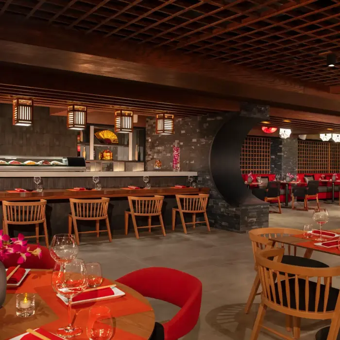 Elegant Japanese restaurant with sushi bar, red and black decor, wooden seating, and warm ambient lighting.