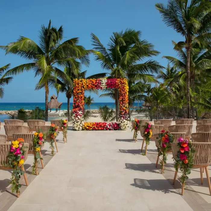 Vibrant beach wedding ceremony setup at Dreams Aventuras with colorful floral arch, palm trees, and ocean view.