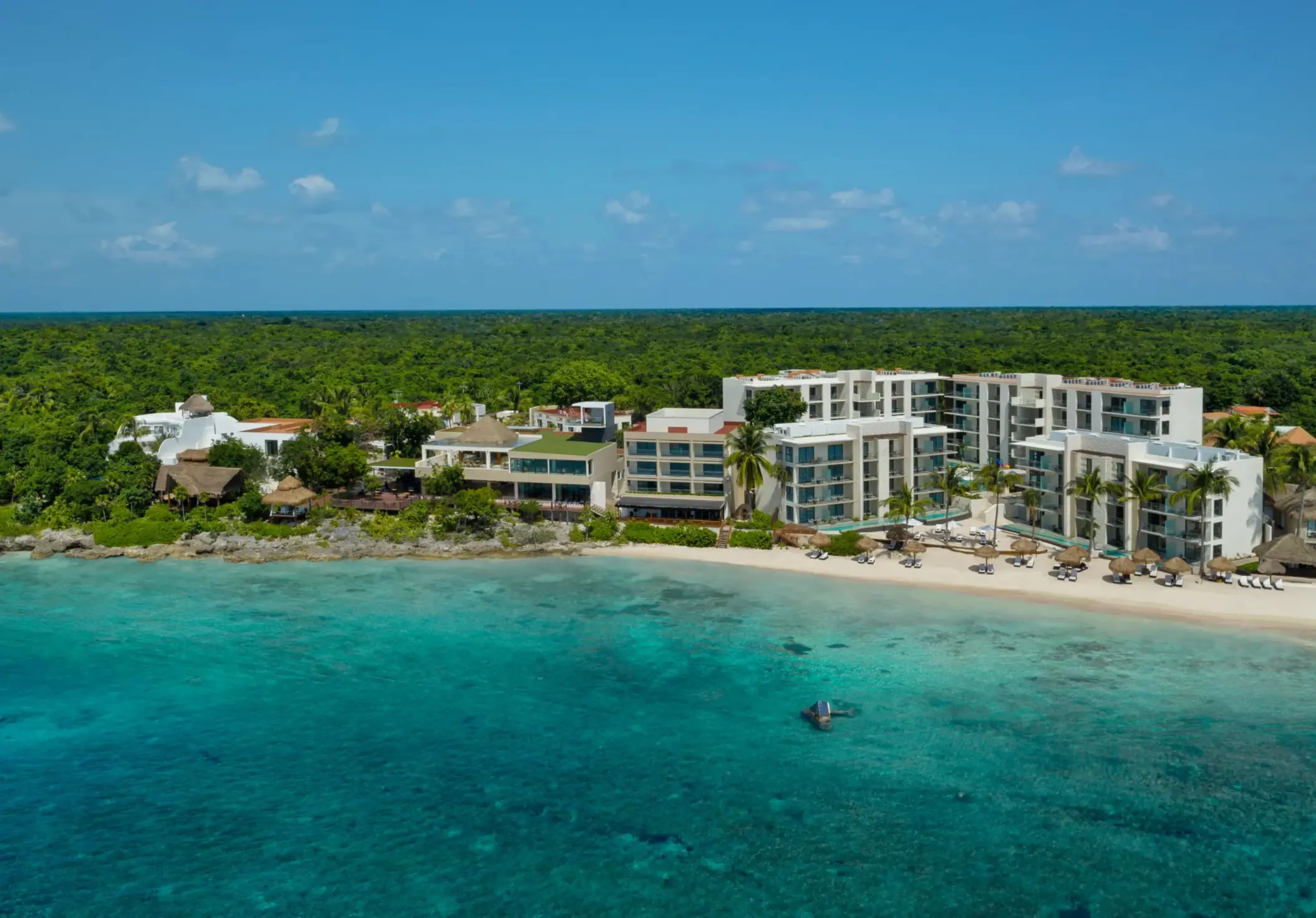 Aerial view of beachfront resort surrounded by lush jungle and turquoise water along rocky coastline.