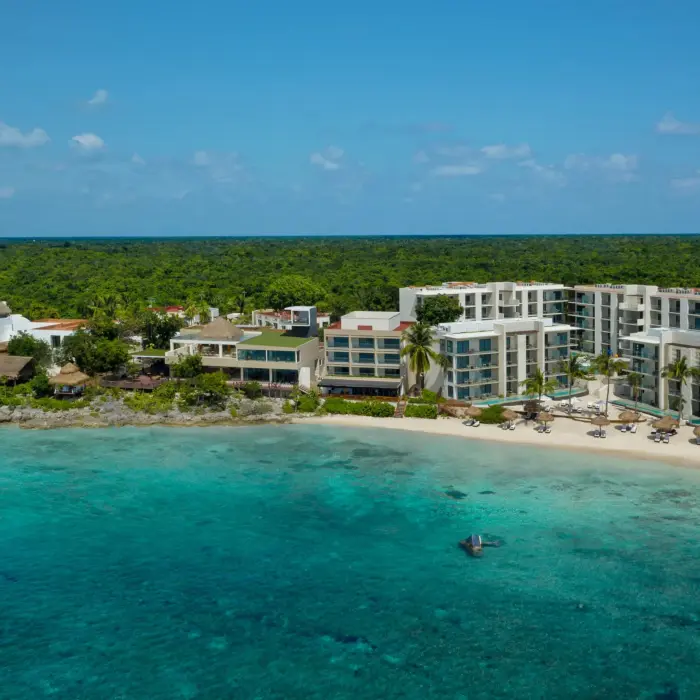 Aerial view of beachfront resort surrounded by lush jungle and turquoise water along rocky coastline.