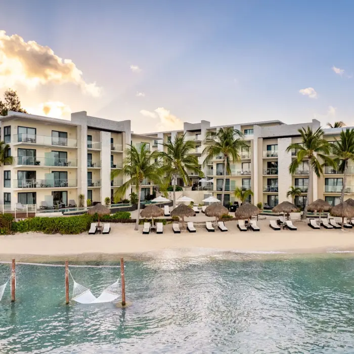 Ocean-facing resort with white sand beach, lounge chairs, and tranquil water framed by tropical trees.