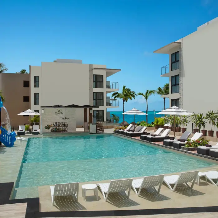 Main resort pool with loungers, umbrellas, splash zone, and Marlin swim-up bar under blue skies.