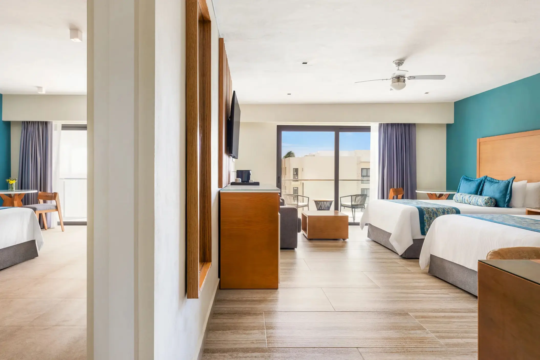 Modern family suite with two beds, balcony seating, and neutral tones enhanced by teal and wood accents.