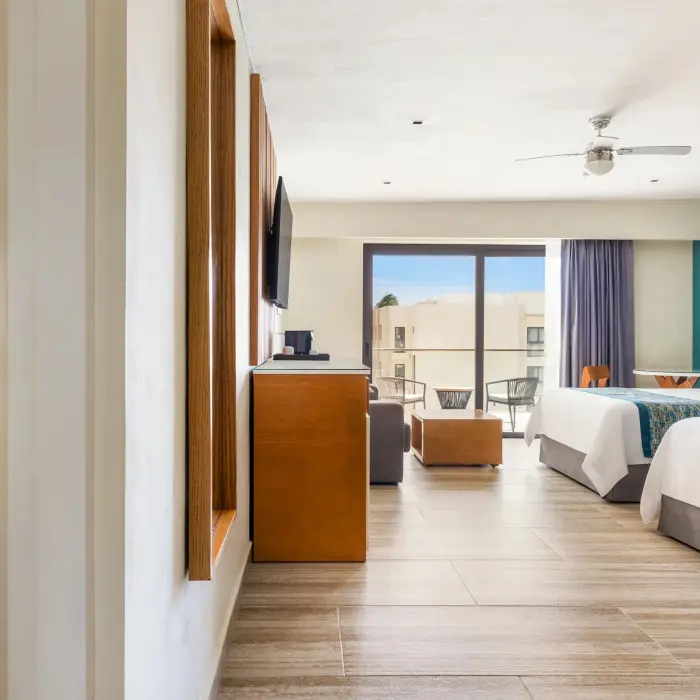 Modern family suite with two beds, balcony seating, and neutral tones enhanced by teal and wood accents.