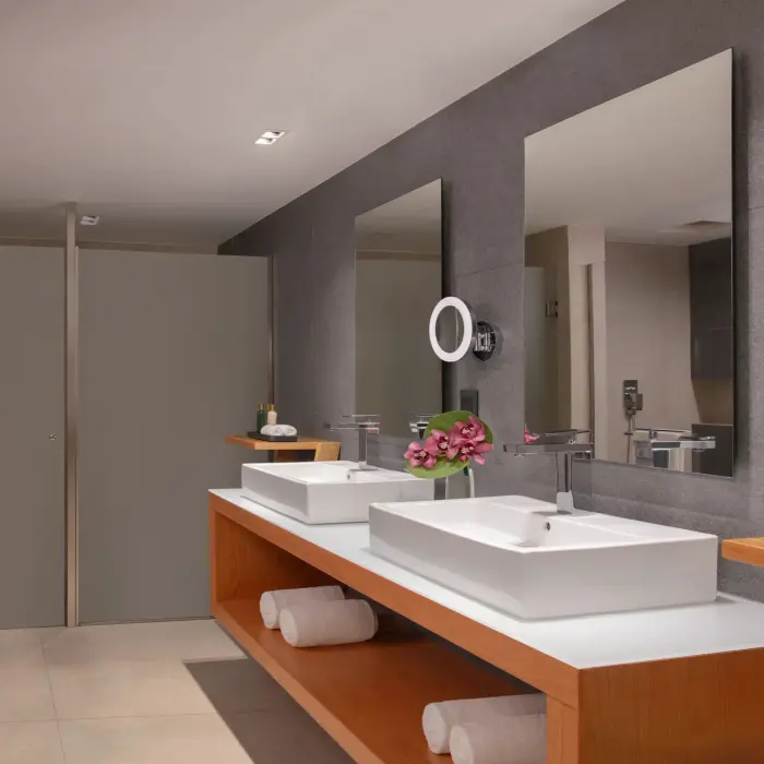 Spacious bathroom with double vanity, modern sinks, soft lighting, and tropical flower arrangement.