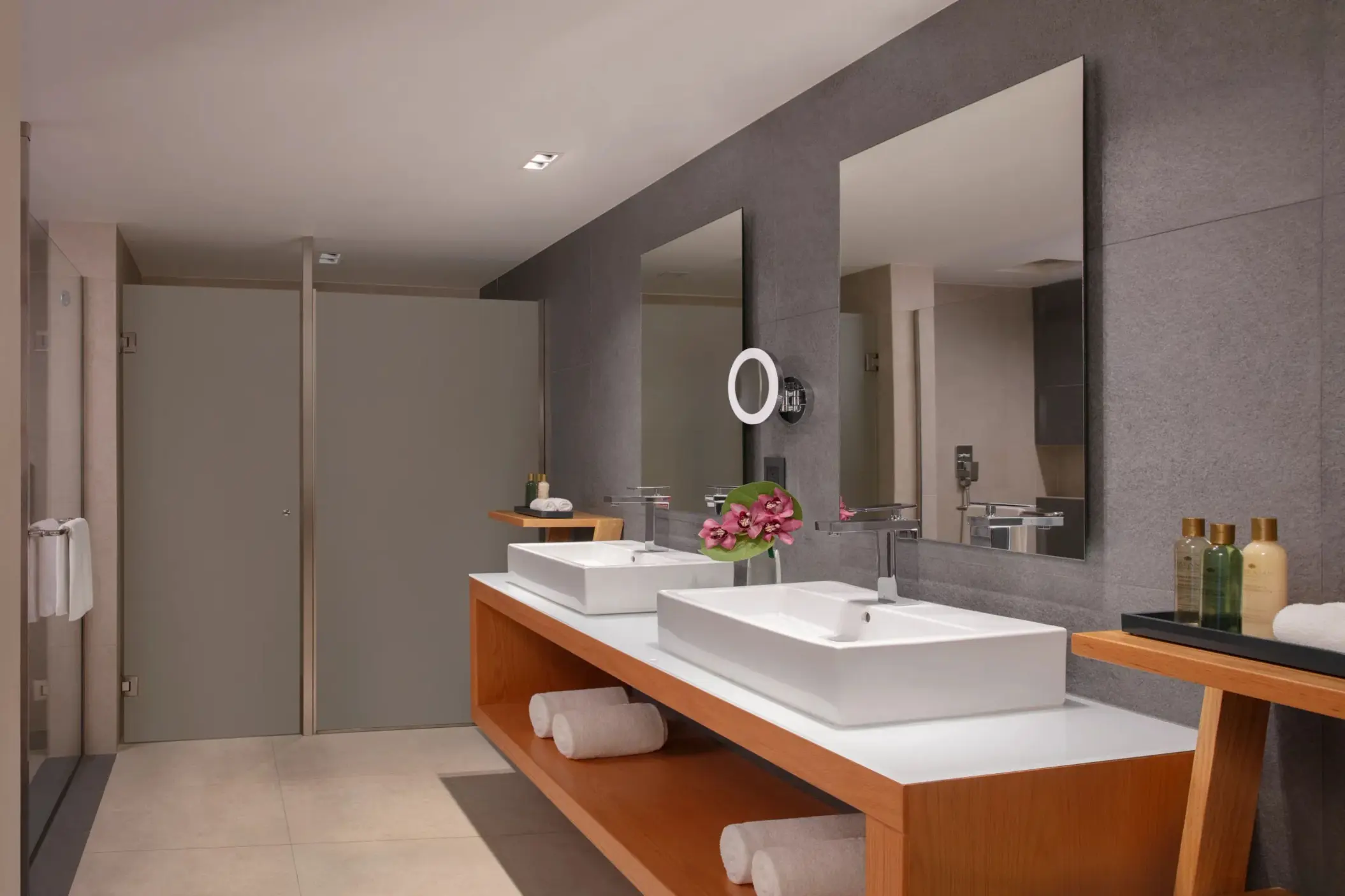 Spacious bathroom with double vanity, modern sinks, soft lighting, and tropical flower arrangement.