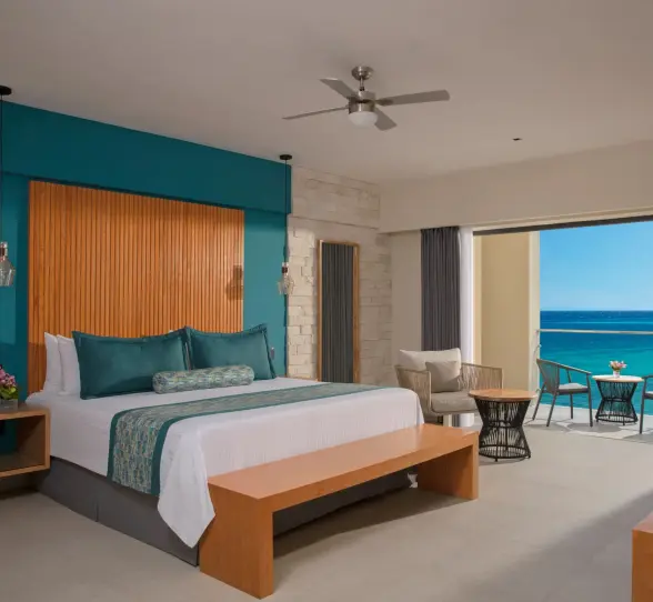 Oceanview suite with king bed, stylish teal accents, sitting area, and private balcony overlooking the sea.