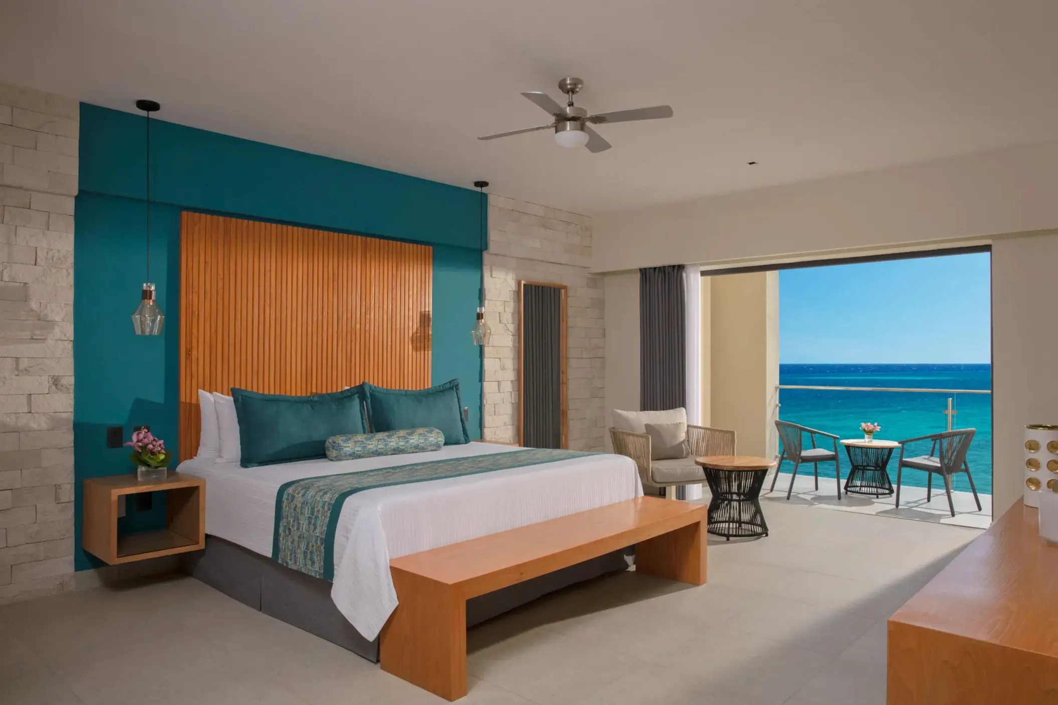 Oceanview suite with king bed, stylish teal accents, sitting area, and private balcony overlooking the sea.