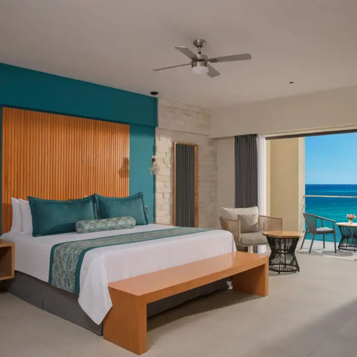 Oceanview suite with king bed, stylish teal accents, sitting area, and private balcony overlooking the sea.