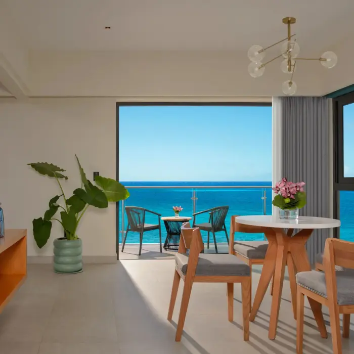 Bright living and dining area with ocean views, modern decor, and balcony seating facing the turquoise sea.