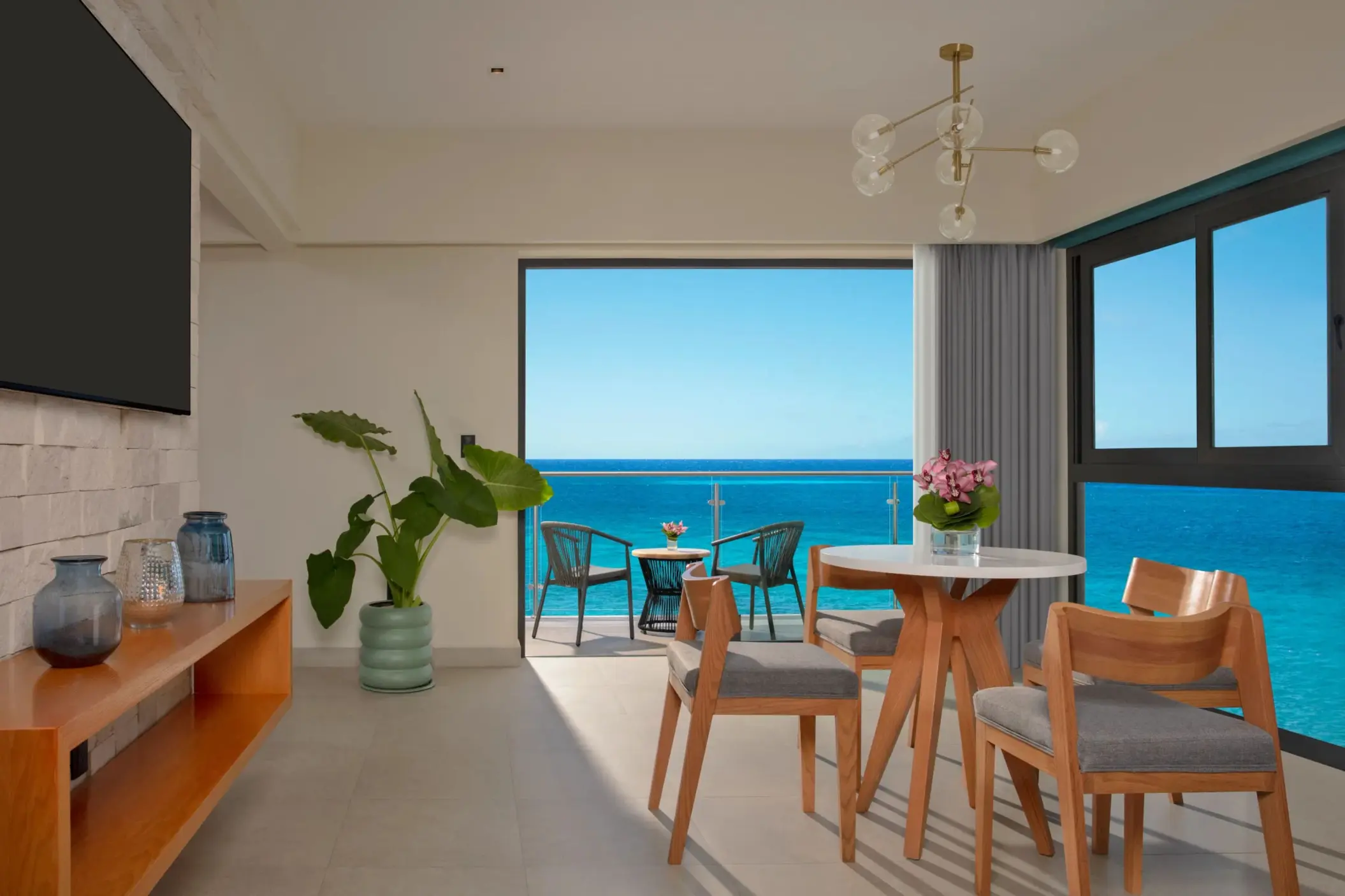 Bright living and dining area with ocean views, modern decor, and balcony seating facing the turquoise sea.