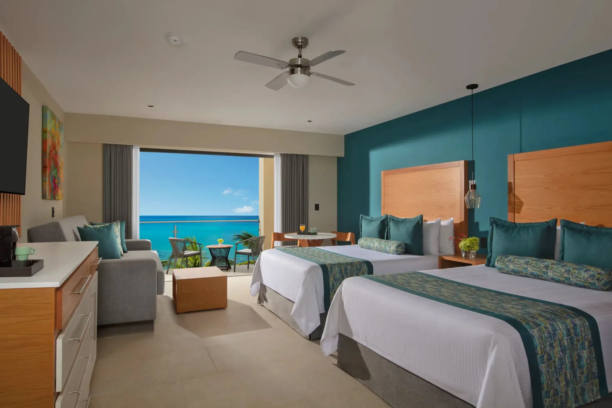Oceanfront room with two beds, teal accents, and private balcony overlooking the Caribbean Sea.