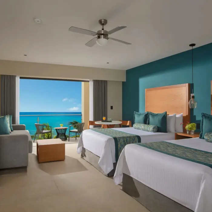 Oceanfront room with two beds, teal accents, and private balcony overlooking the Caribbean Sea.