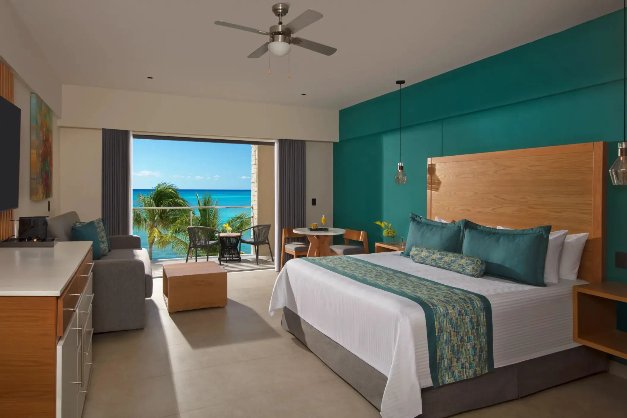 Oceanfront suite with king bed, sitting area, and balcony with panoramic turquoise water views.