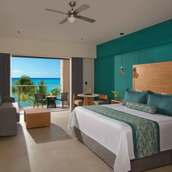 Oceanfront suite with king bed, sitting area, and balcony with panoramic turquoise water views.