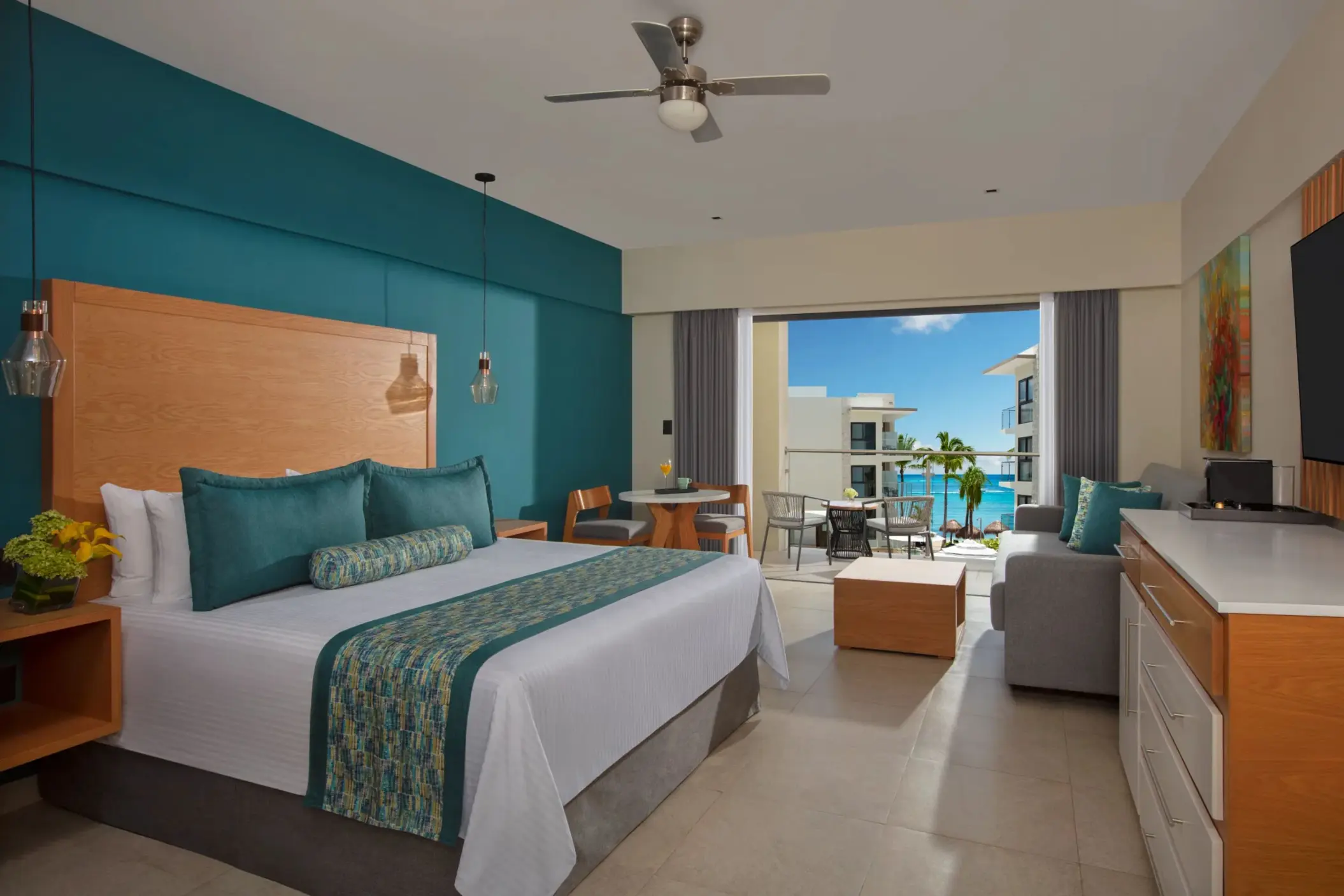 Ocean view suite featuring king bed, lounge space, and balcony with seating and vibrant sea views.